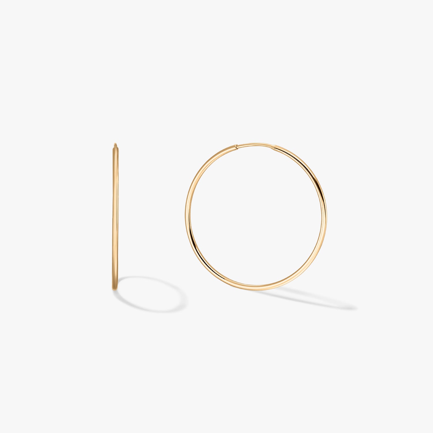 Pair of medium 14K yellow gold hoop earrings on a white background, one shown front-facing and one in side profile.