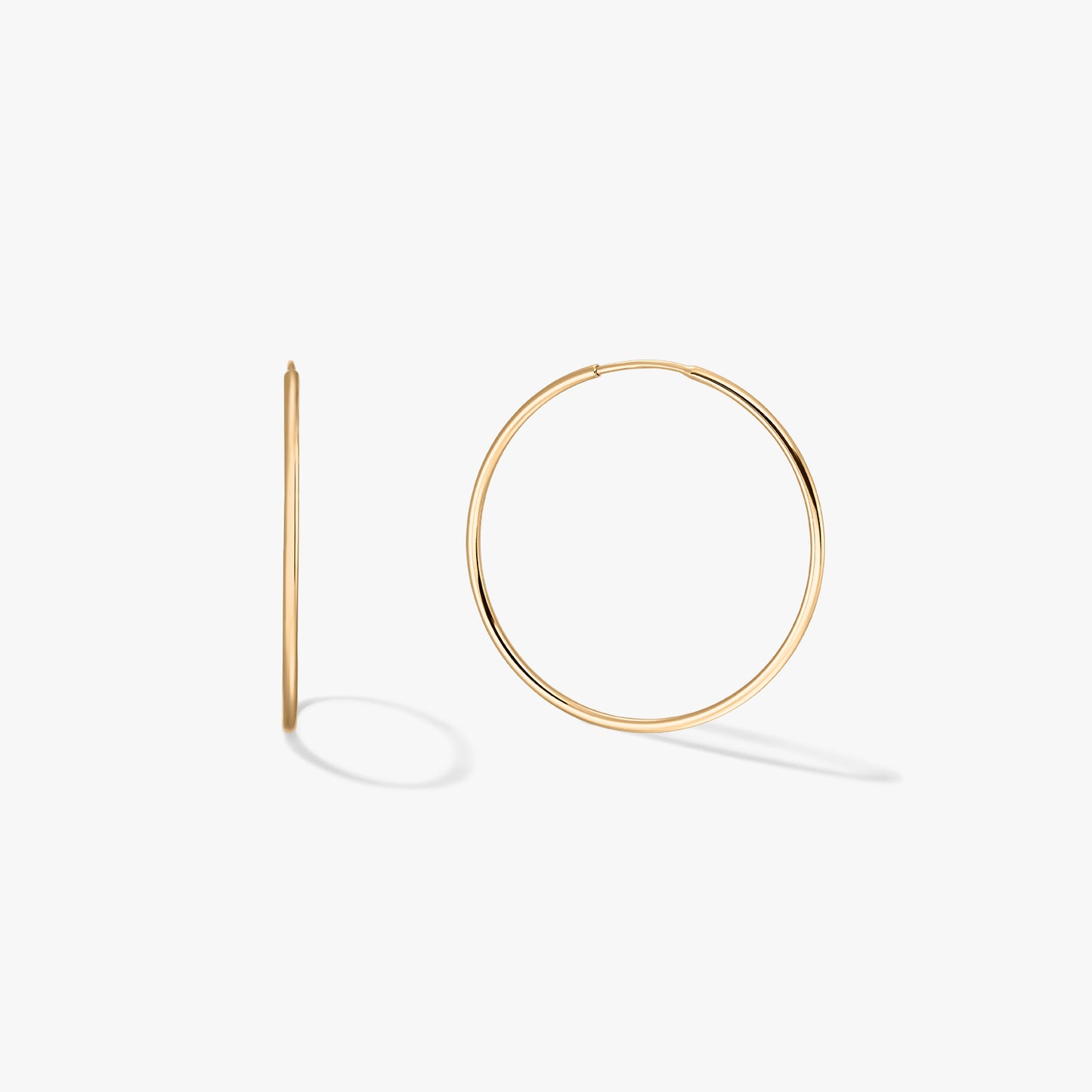 Pair of medium 14K yellow gold hoop earrings on a white background, one shown front-facing and one in side profile.