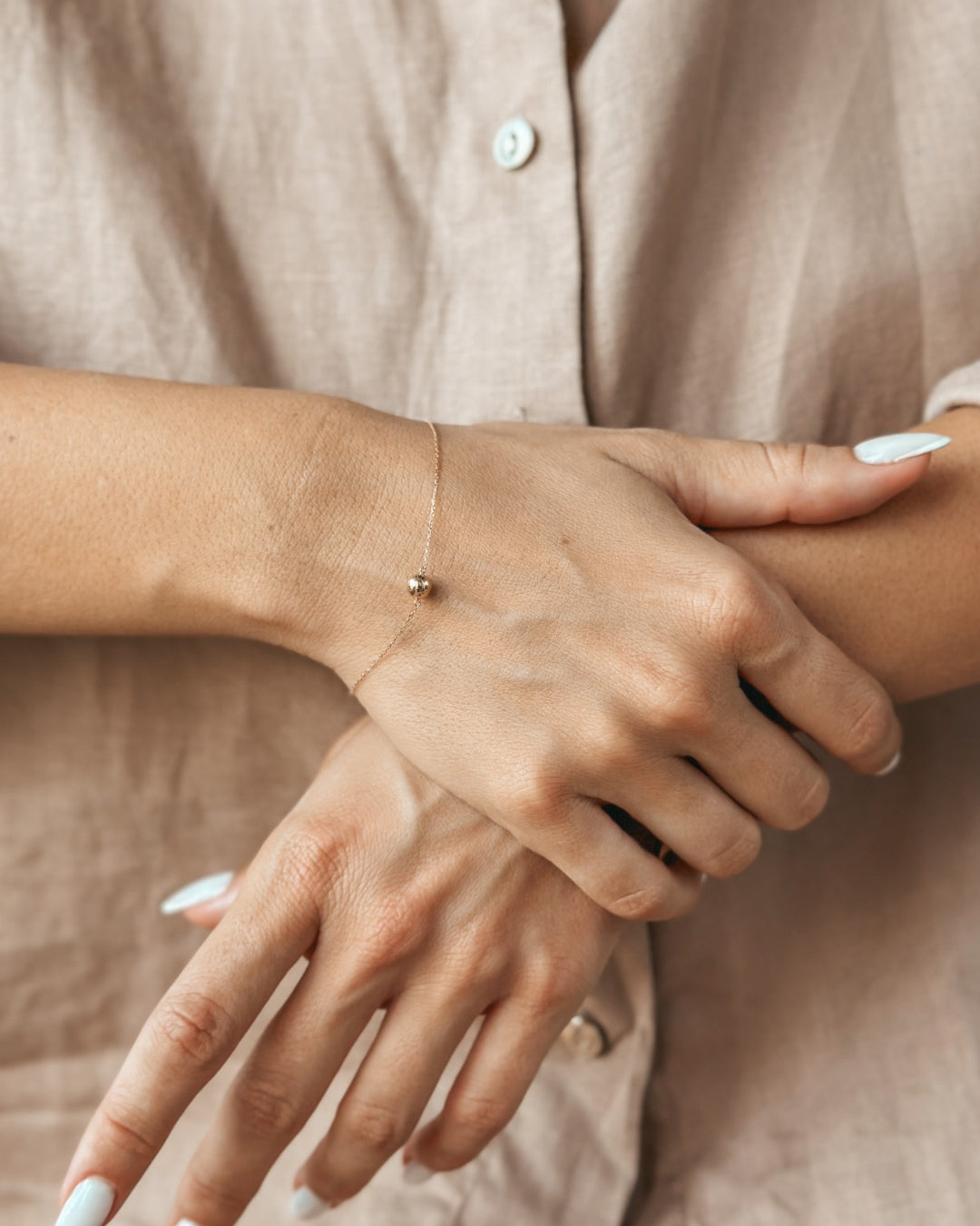 Close-up of a person's hands wearing a delicate gold bracelet.