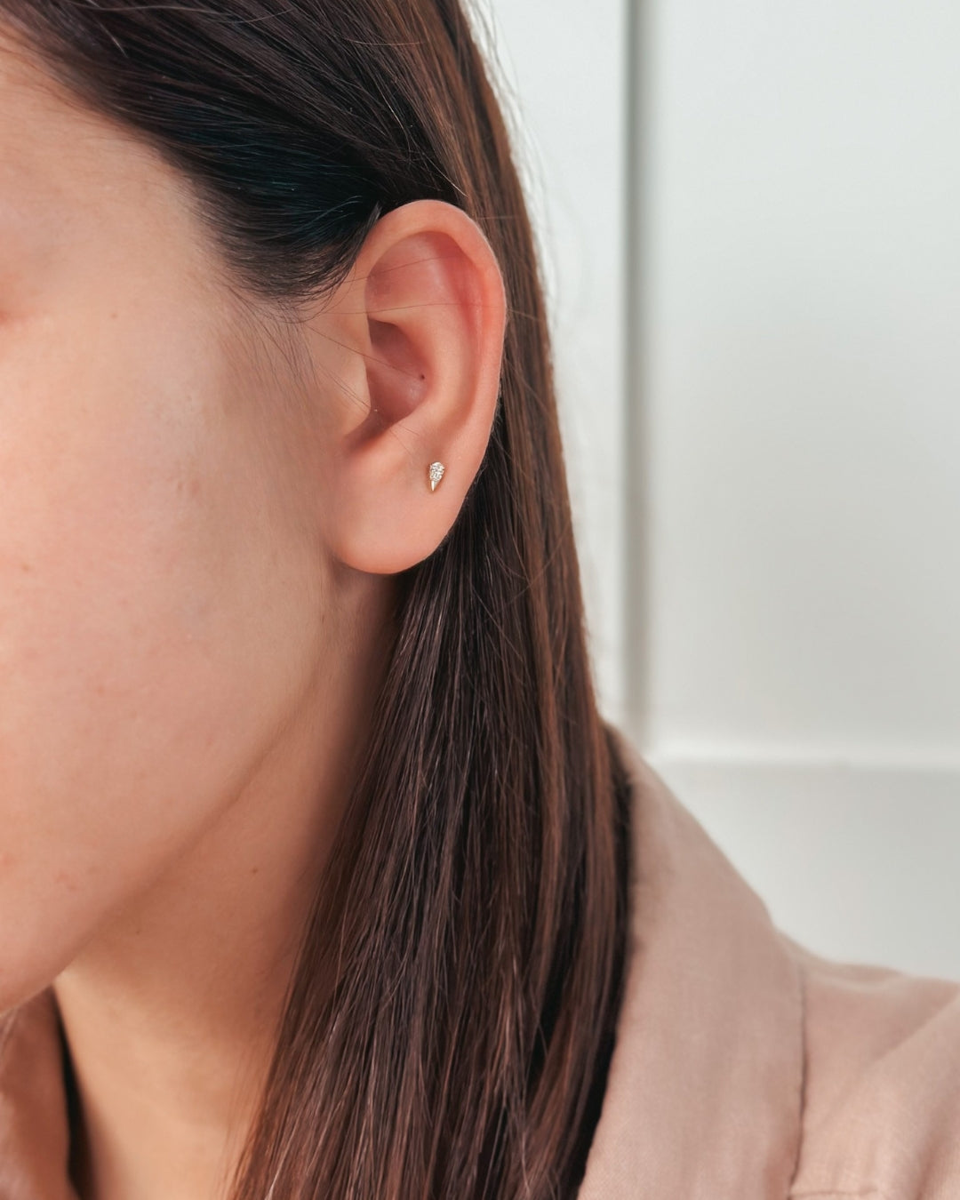 Close-up of a person's ear wearing a small earring against a light background.