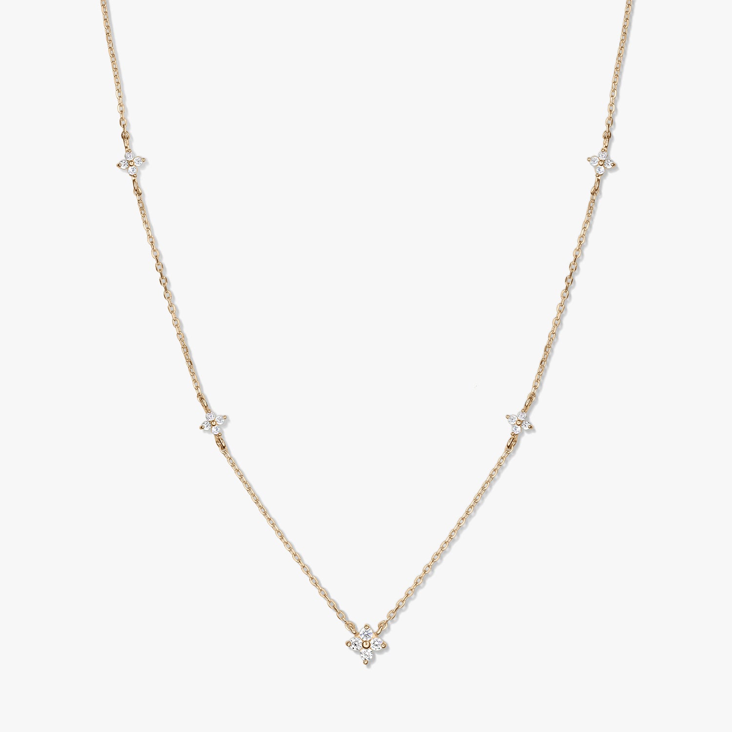 Delicate 14K yellow gold station necklace with small white zirconia clover motifs on a fine chain, photographed on a white background.