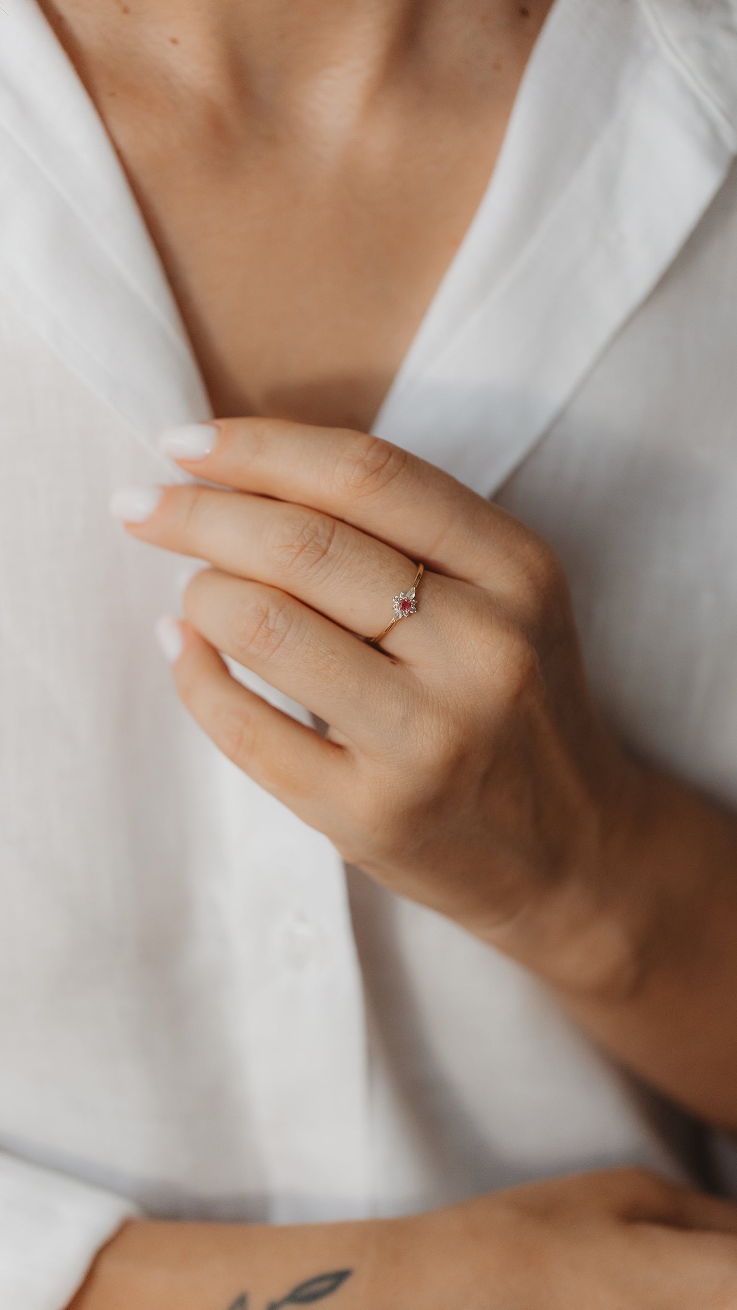 Close-up of a hand wearing a delicate yellow gold ring with a pink tourmaline center and a halo of white sapphires.