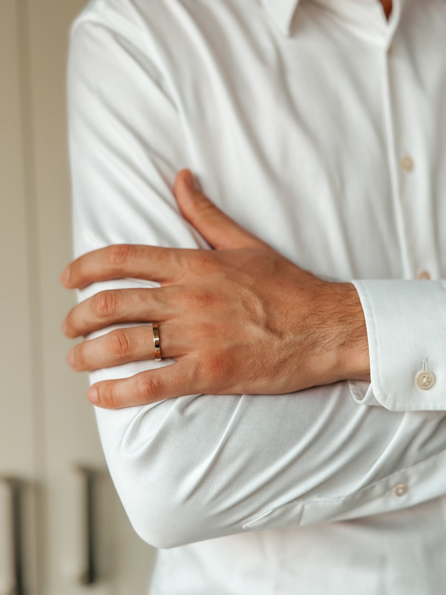Close-up of a man's arm wearing a simple gold wedding band on a white shirt.