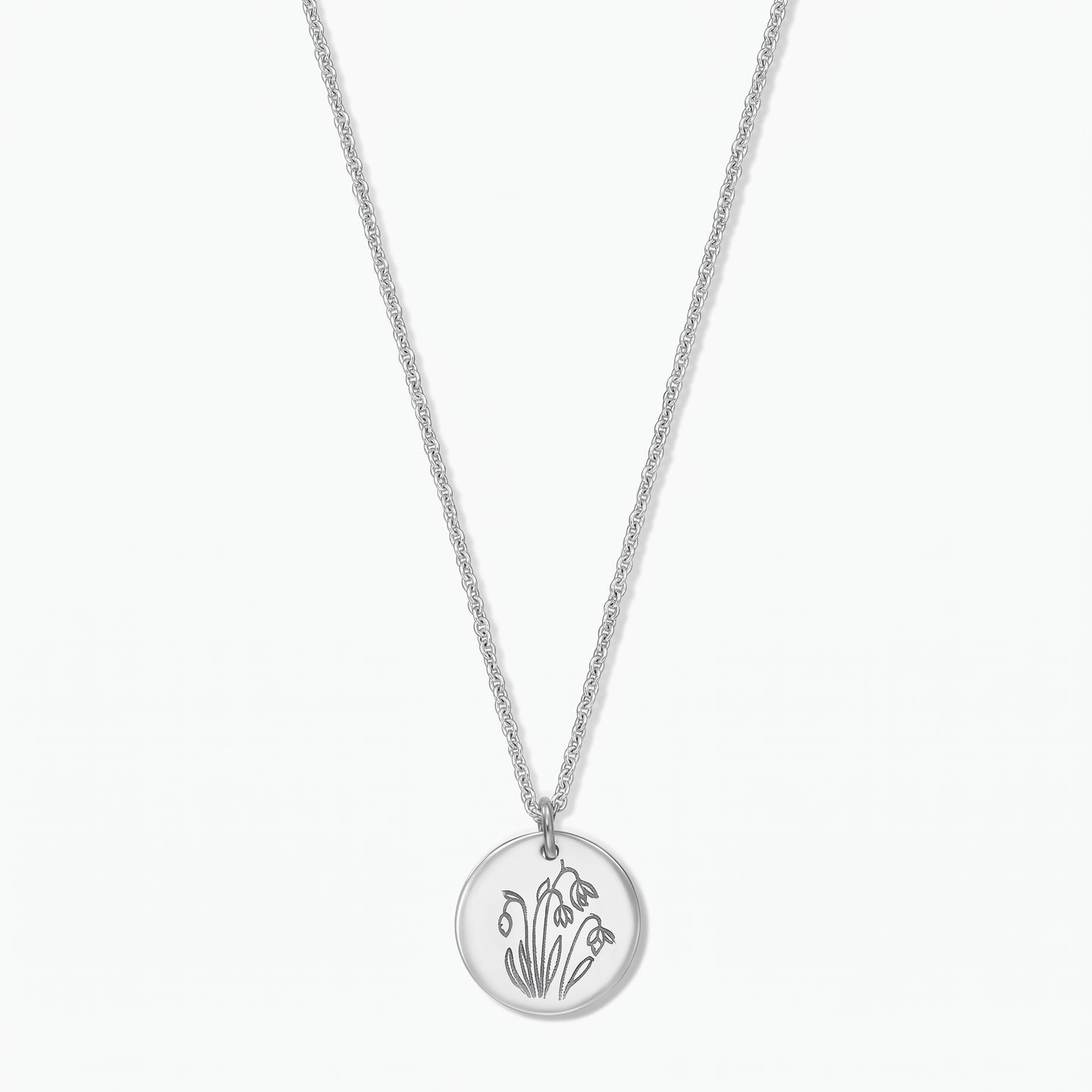 Sterling silver birthflower necklace with a round disc pendant engraved with January snowdrops on a fine chain, isolated on a white background.