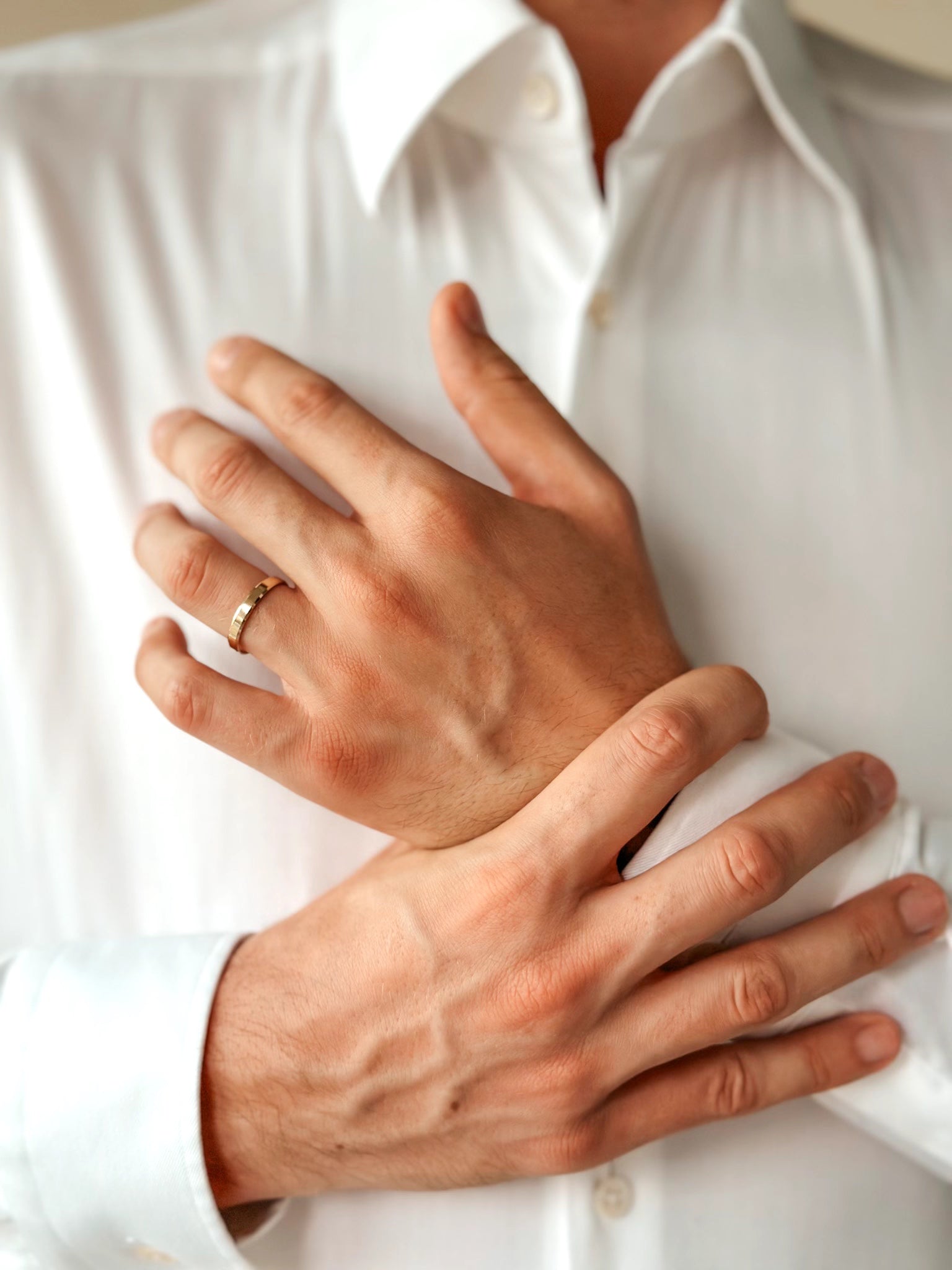 Close-up of hands wearing a gold wedding band against a white shirt backdrop.