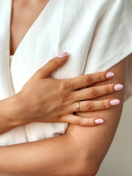 Close-up of a hand with a gold wedding band and manicured nails on a white fabric background.