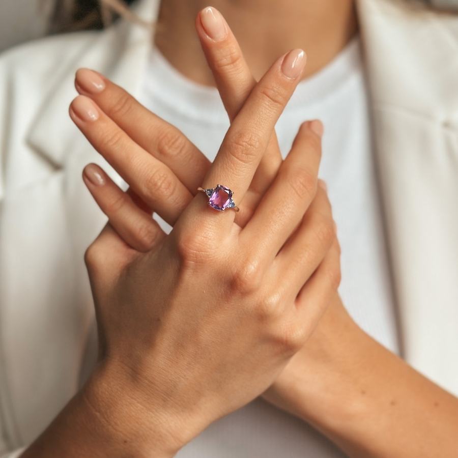 Hands crossed displaying a silver ring with amethyst and tanzanite stones.