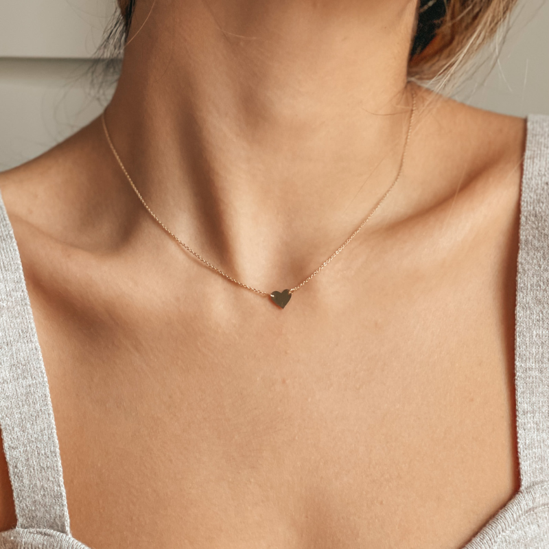 A woman's neck wearing a delicate 14K gold heart necklace.