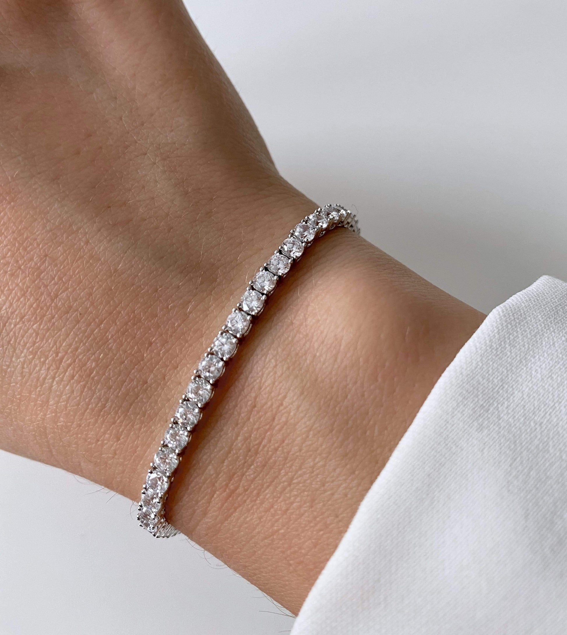 Close-up of a wrist wearing a silver tennis bracelet with zirconia stones.