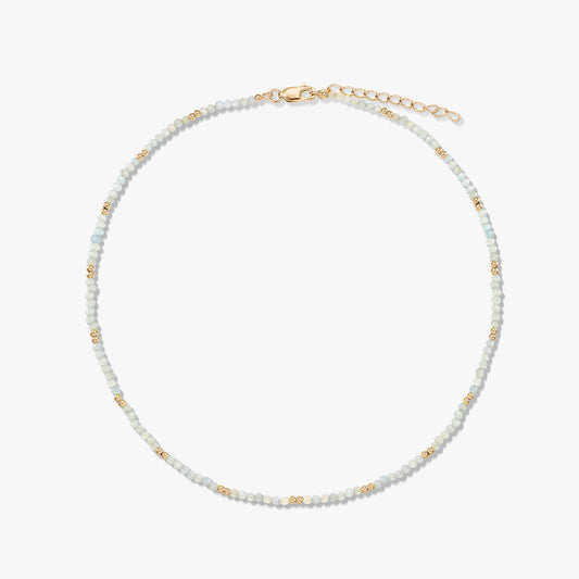 Delicate beaded moonstone necklace with small gold spacer beads and a gold‑plated sterling silver lobster clasp and extender, arranged in a circle on a white background.