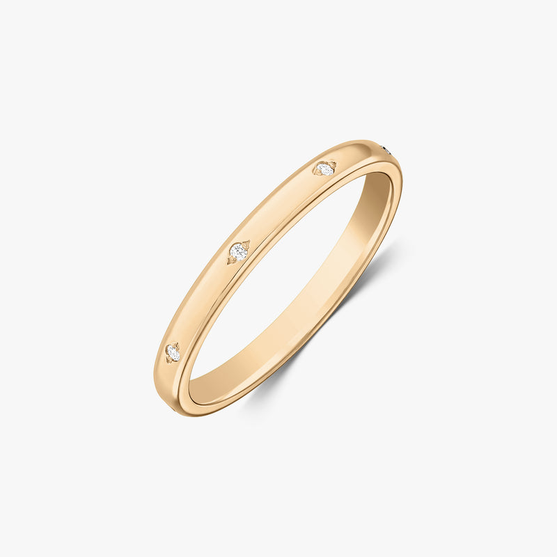 Angled studio shot of a slim 14K yellow gold wedding band with small flush-set diamond accents on a white background.