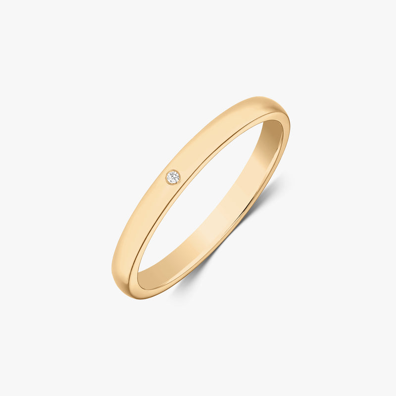 Slim 14k yellow gold wedding band with a small round diamond flush set, angled view on a white background.
