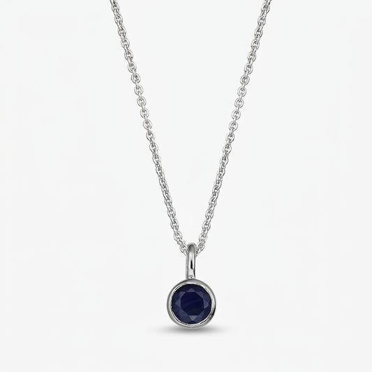 Sterling silver birthstone necklace with a small round bezel‑set dark blue sapphire pendant on a fine chain, isolated on white.