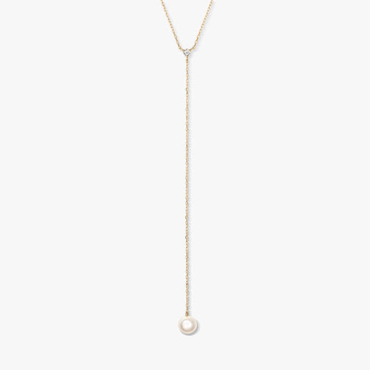 Minimalista arany lariat nyaklánc egyetlen kerek fehér gyöngyfüggővel és apró díszkővel, fehér háttéren középre helyezve.
