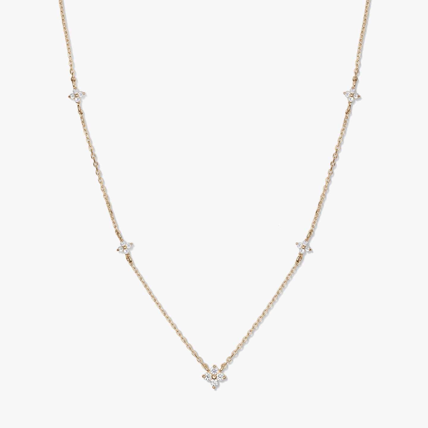 Delicate 14K yellow gold station necklace with small white zirconia clover motifs on a fine chain, photographed on a white background.
