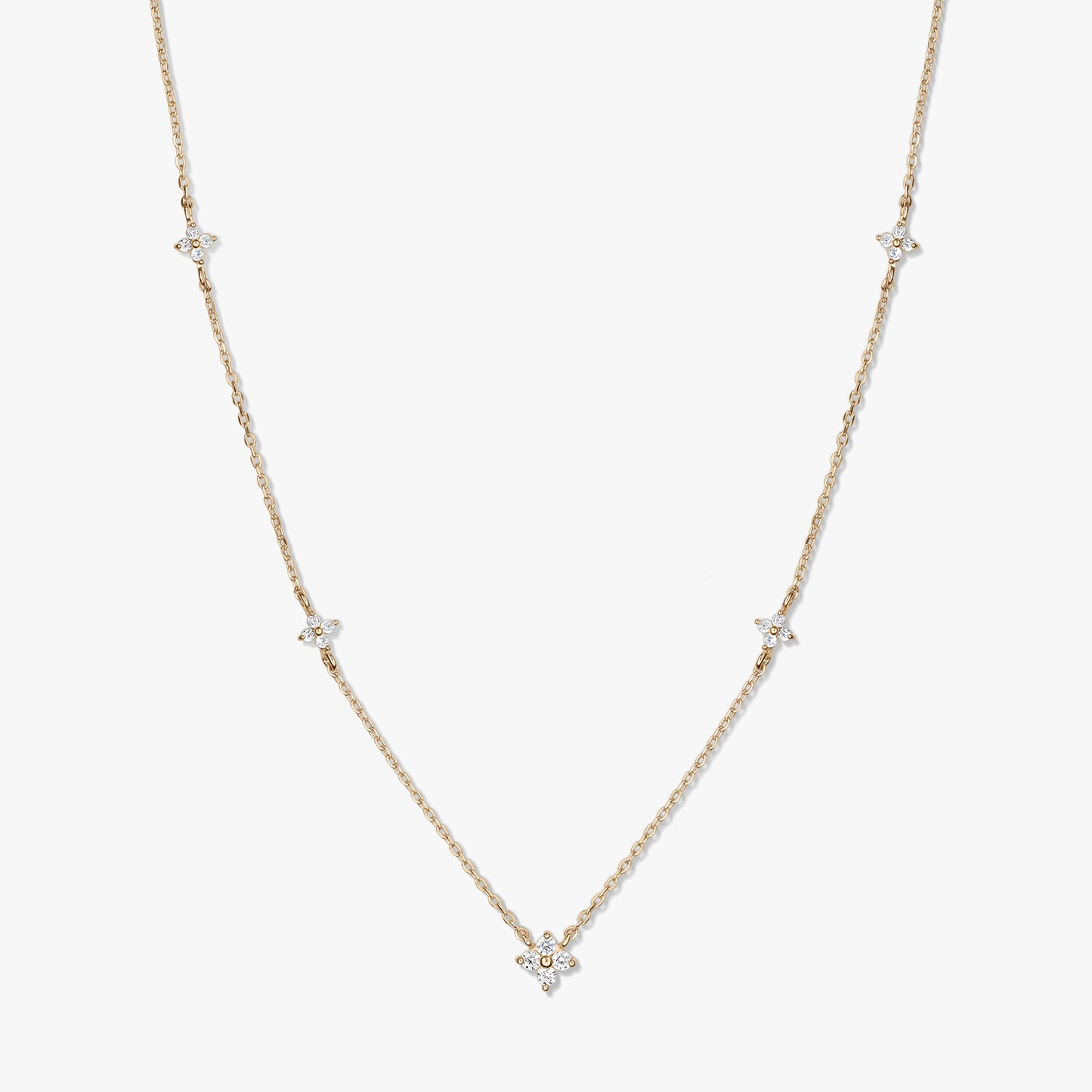 Delicate 14K yellow gold station necklace with small white zirconia clover motifs on a fine chain, photographed on a white background.
