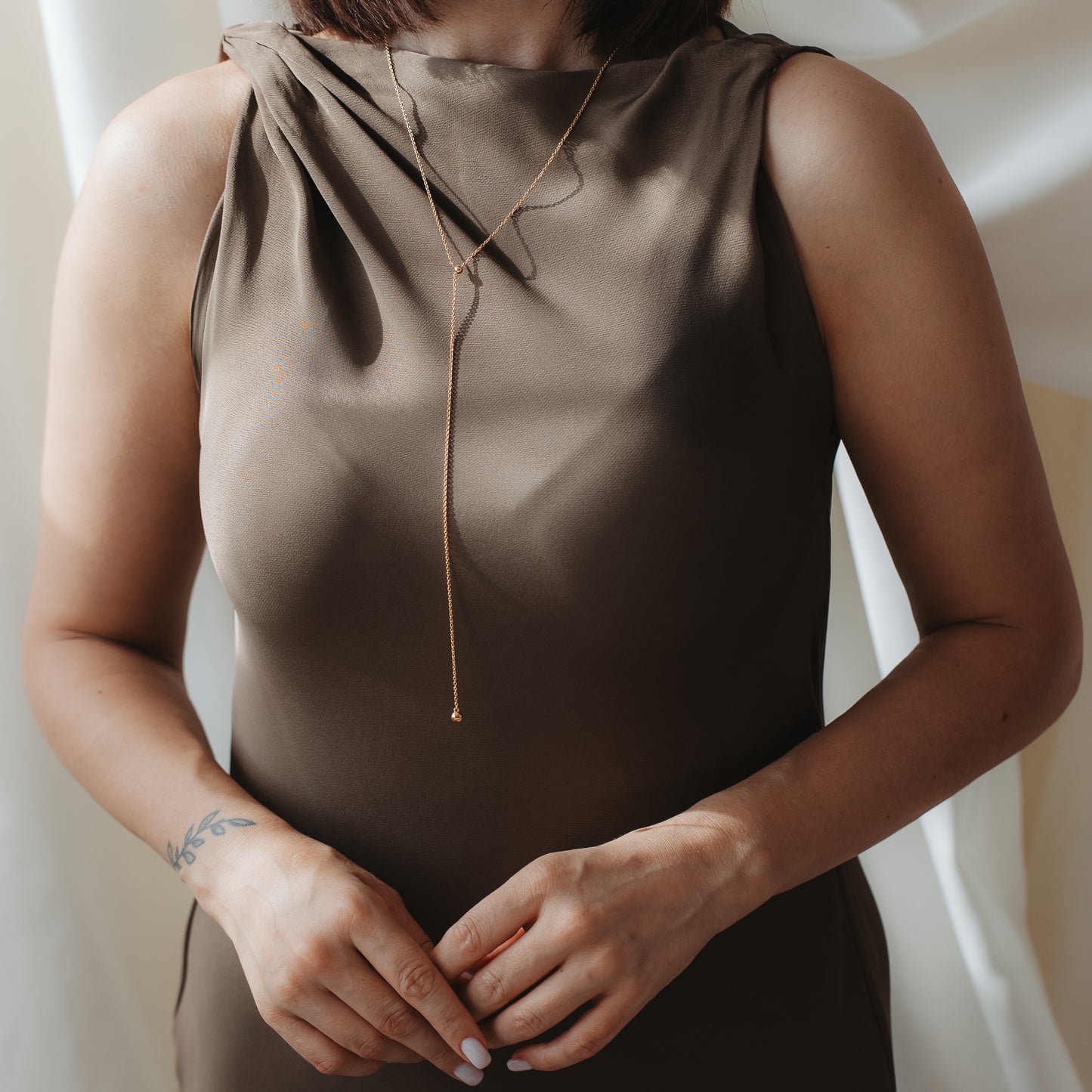 Close-up of a person wearing a brown satin dress and an adjustable gold‑plated sterling silver lariat necklace with a small cultured pearl drop.