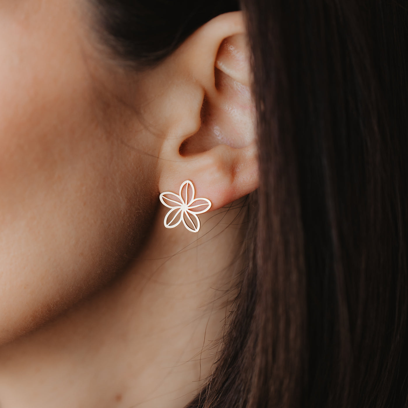 Close-up of an ear wearing a delicate 14K yellow gold openwork flower stud earring.