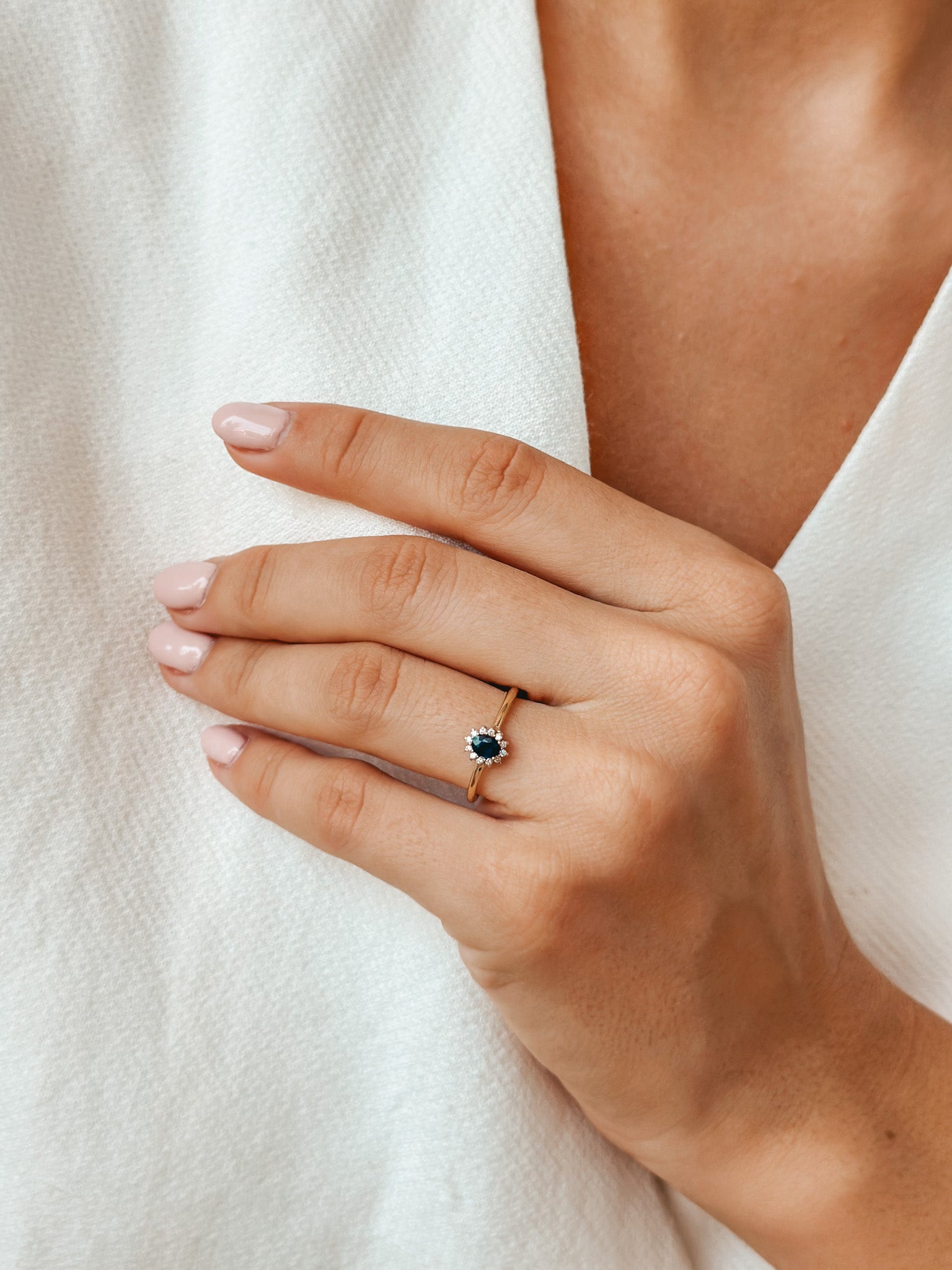 Close-up of a hand wearing a gold ring with a sapphire and diamonds