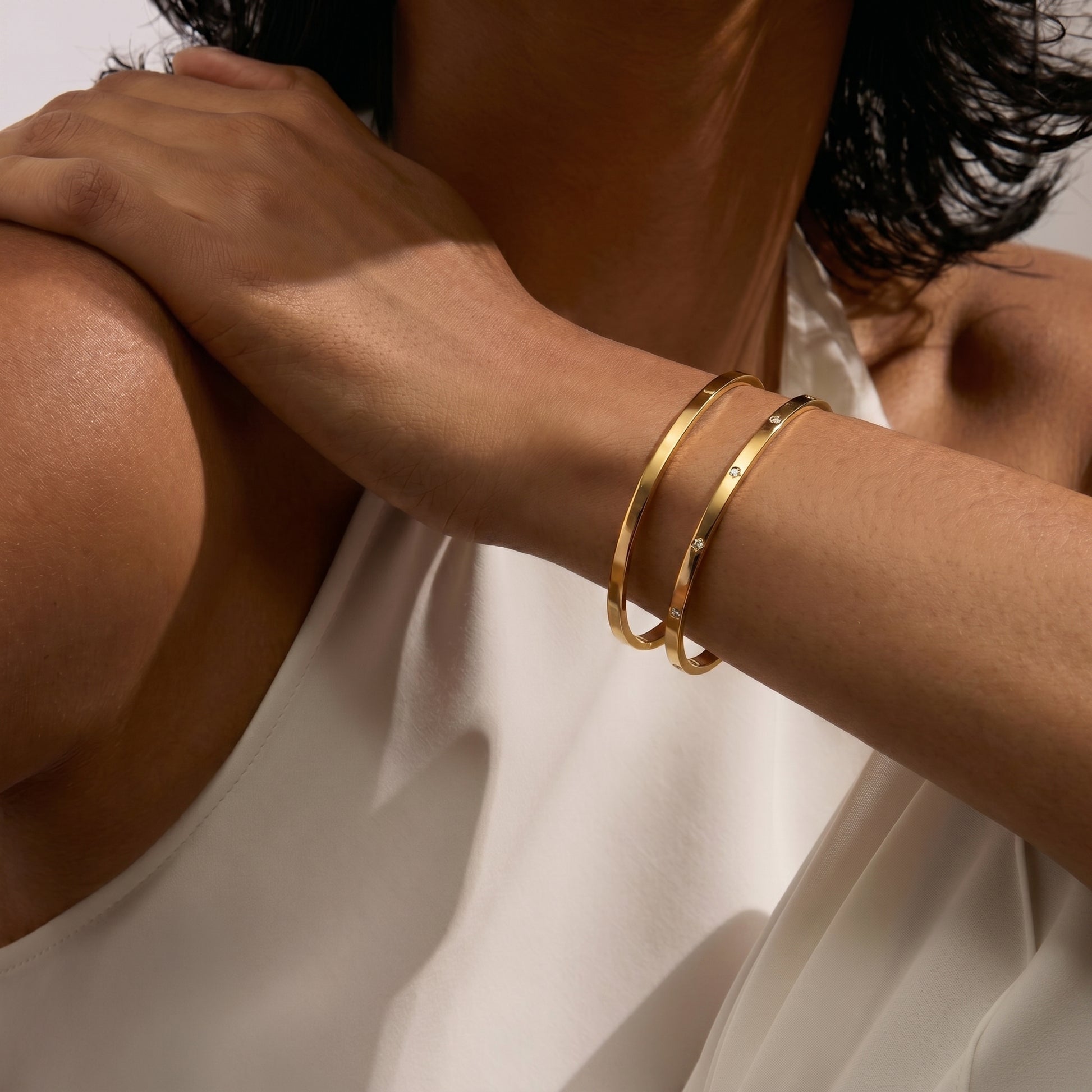 Close-up of a person's arm wearing two gold bangle bracelets on a white background.