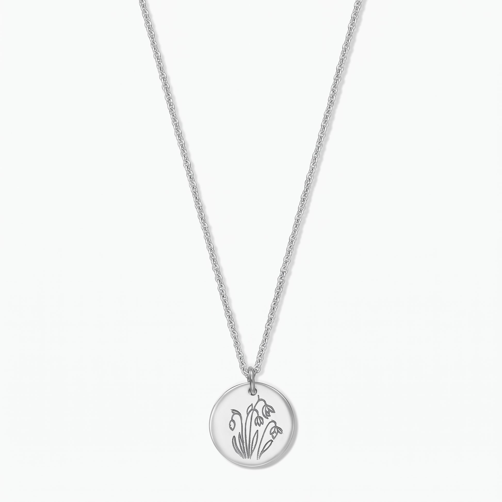 Sterling silver birthflower necklace with a round disc pendant engraved with January snowdrops on a fine chain, isolated on a white background.