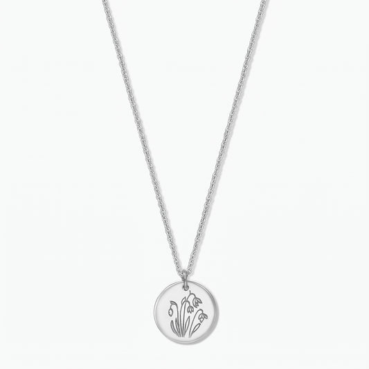 Sterling silver birthflower necklace with a round disc pendant engraved with January snowdrops on a fine chain, isolated on a white background.