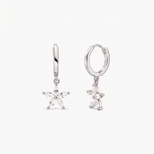 Pair of sterling silver huggie hoop earrings with dangling five‑petal blossom charms set with white topaz on a white background.